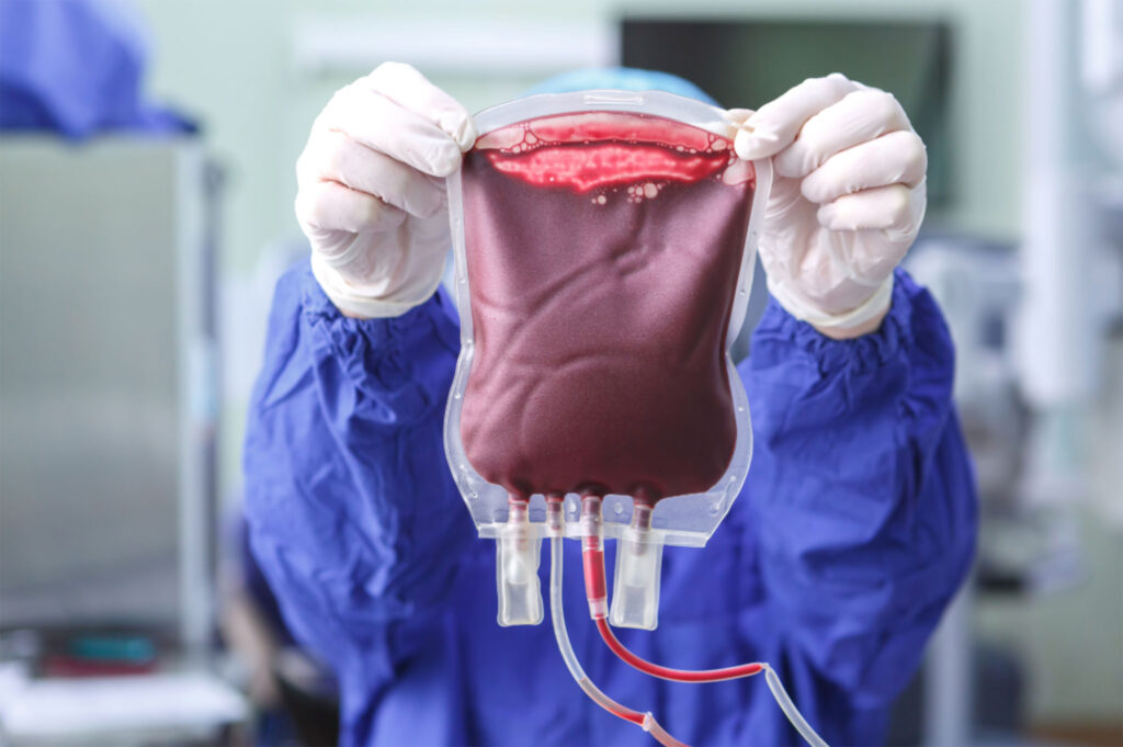 A healthcare professional in blue scrubs holding a bag of blood.