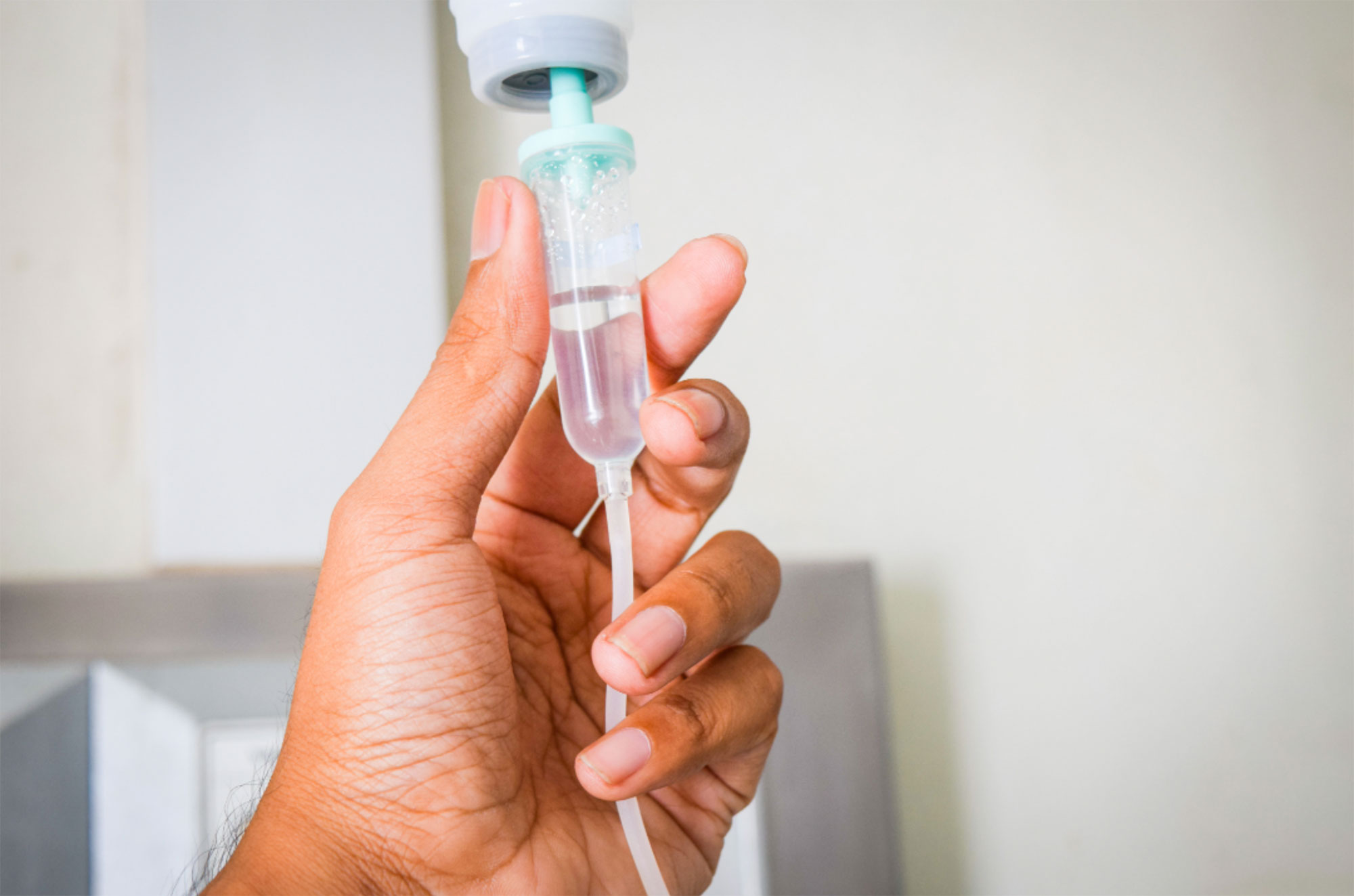 A hand adjusts a medical IV drip chamber with clear liquid inside.