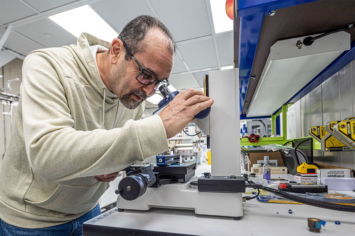 A man in a laboratory examining a specimen through a microscope, focused on his research and analysis.