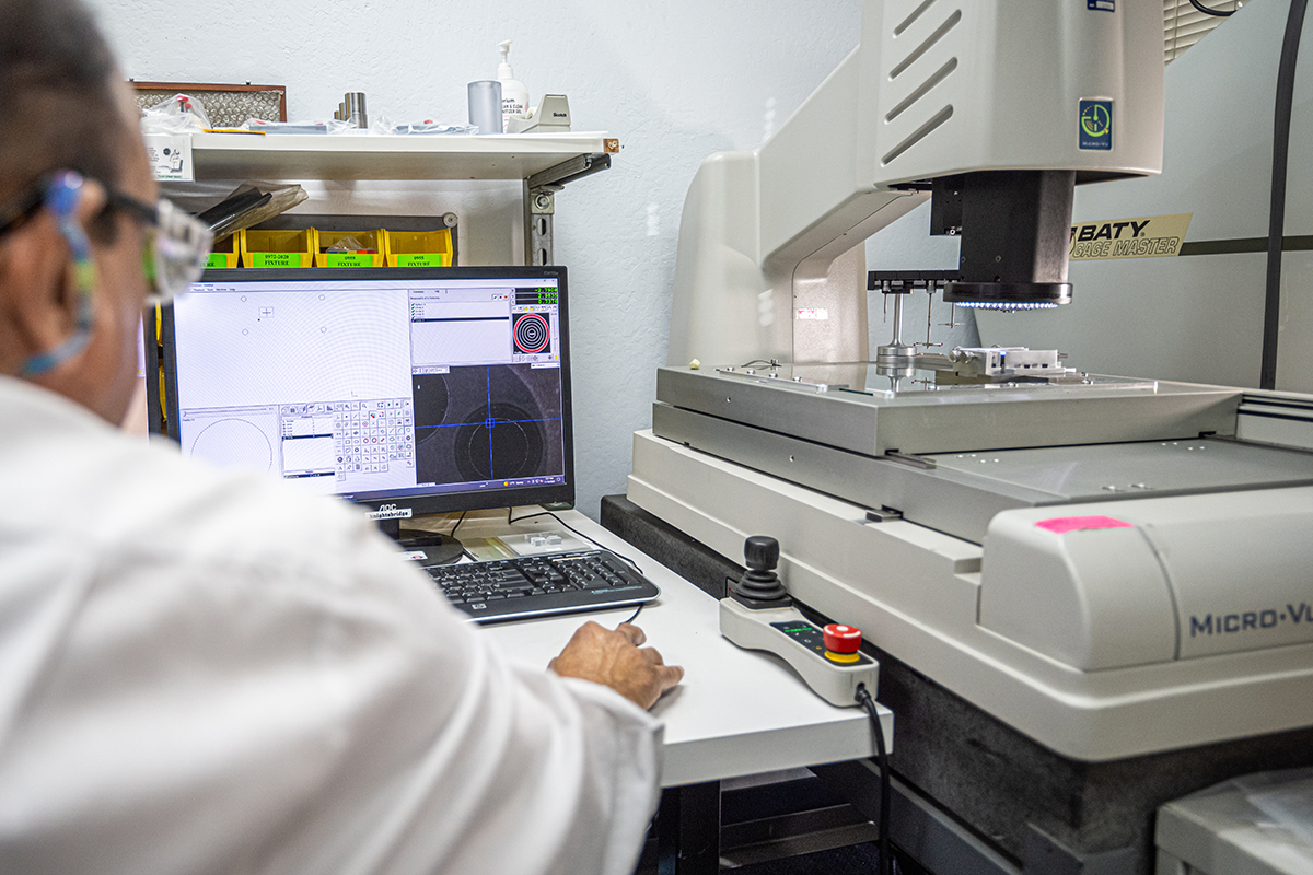an employee in a white lab coat, looking at the computer