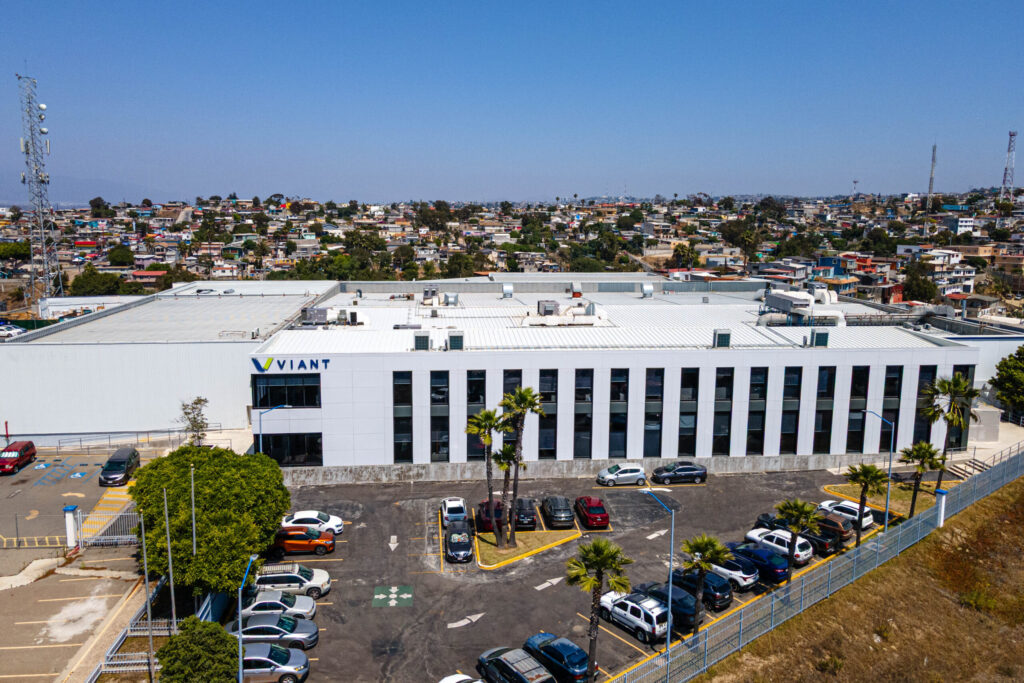 Aerial view of the Viant medical manufacturing facility in Tijuana, Mexico, featuring a large white modern building with blue branding and a surrounding parking area.
