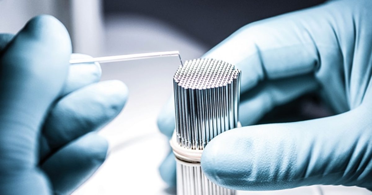 A person with a blue glove is holding a metal tube